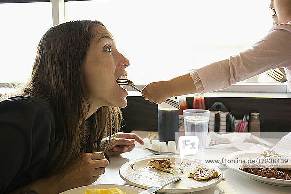 Toddler daughter feeding mother from fork in diner