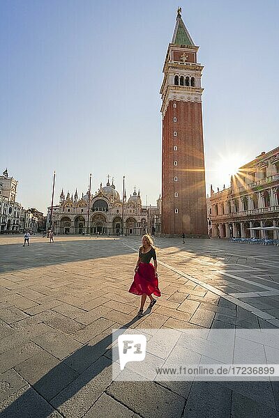 Junge Frau  Touristin mit rotem Kleid am Markusplatz  Sonne scheint auf Markusplatz mit Campanile di San Marco  Venedig  Venetien  Italien  Europa