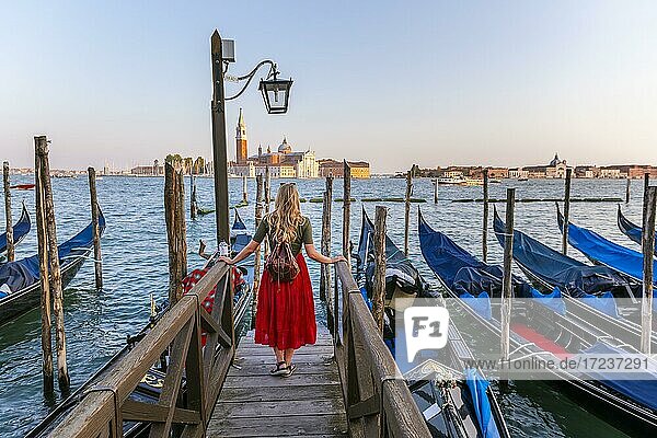 Young woman with red dress on a jetty  Venetian gondolas  in the back church San Giorgio Maggiore  Venice  Veneto  Italy  Europe