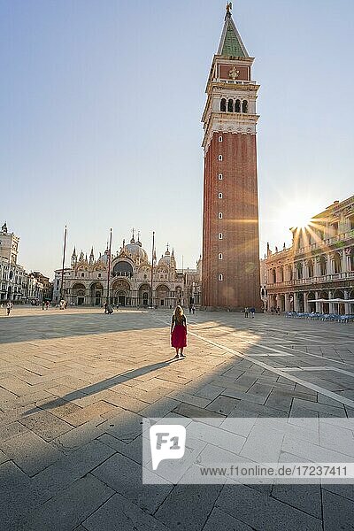 Junge Frau  Touristin mit rotem Kleid am Markusplatz  Sonne scheint auf Markusplatz mit Campanile di San Marco  Venedig  Venetien  Italien  Europa