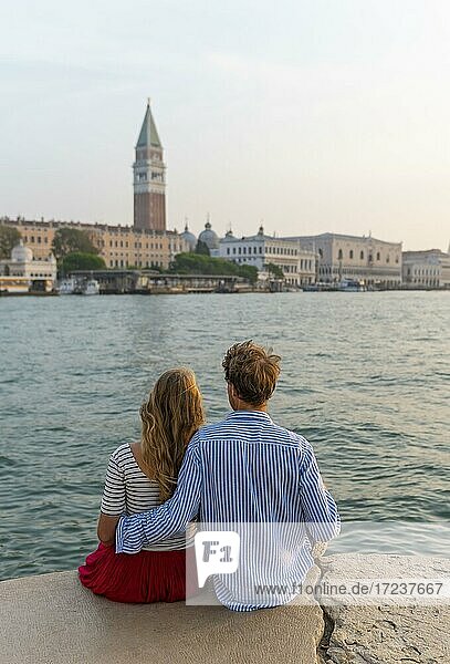 Junges Paar sitzt am Meer und genießt Blick auf Markusplatz mit Campanile di San Marco  Venedig  Venetien  Italien  Europa