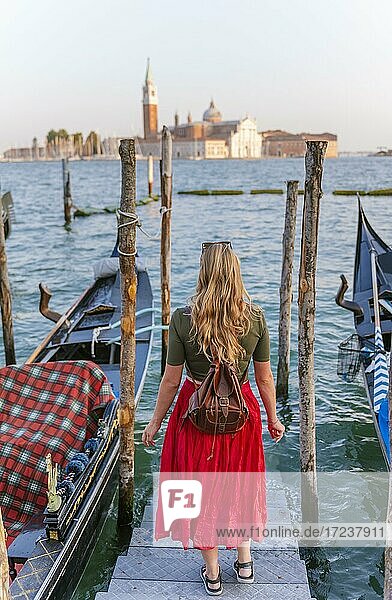 Junge Frau mit rotem Kleid auf einem Bootssteg  venezianische Gondeln  hinten Kirche San Giorgio Maggiore  Venedig  Venetien  Italien  Europa