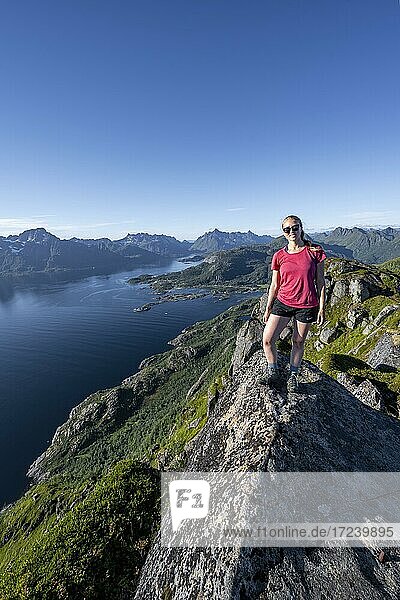 Junge Wanderin steht auf Felsen  Fjord Raftsund und Berge  Blick vom Gipfel des Dronningsvarden oder Stortinden  Vesterålen  Norwegen  Europa