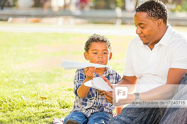 Glücklicher afrikanischer amerikanischer Vater und gemischter Rasse Sohn spielen mit Papierflugzeugen im Park