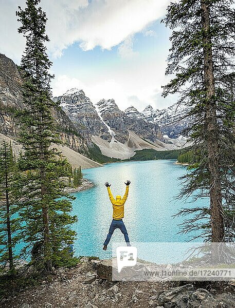 Junger Mann springt in die Luft und streckt die Arme in die Luft  Bergkette hinter türkisfarbenem Gletschersee  Moraine Lake  Valley of the Ten Peaks  Rocky Mountains  Banff-Nationalpark  Provinz Alberta  Kanada  Nordamerika