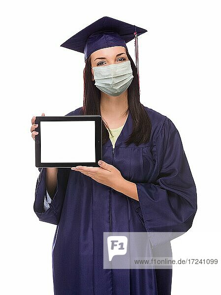 Graduating female wearing medical face mask and cap and gown holding blank computer tablet isolated on a white background
