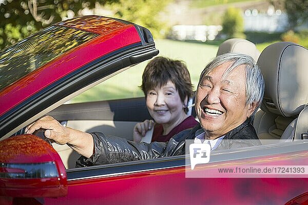 Attractive happy chinese couple enjoying an afternoon drive in their convertible
