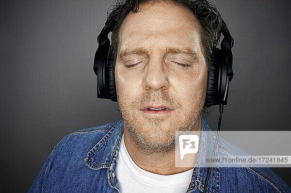 Mann mit geschlossenen Augen und Kopfhörern genießt seine Musik vor einem grauen Hintergrund