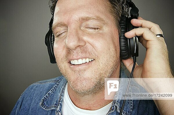 Mann mit Kopfhörern genießt seine Musik vor einem grauen Hintergrund
