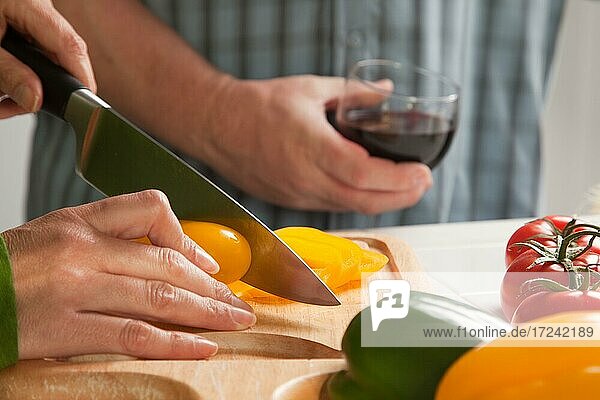 Woman slicing vegetables on cutting board while man enjoys a glass of red wine