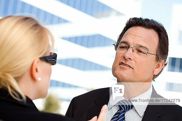 Aufmerksamer  gutaussehender Geschäftsmann in Anzug und Krawatte im Gespräch mit einer Kollegin im Freien