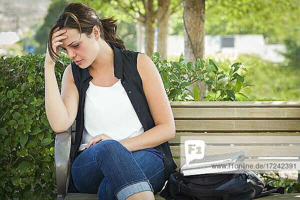 Depressed young woman sitting on bench outside at a park