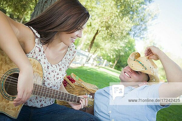 Happy attractive mixed-race couple with guitar and cowboy hat in the park