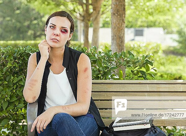 Sad bruised and battered young woman sitting on bench outside at a park