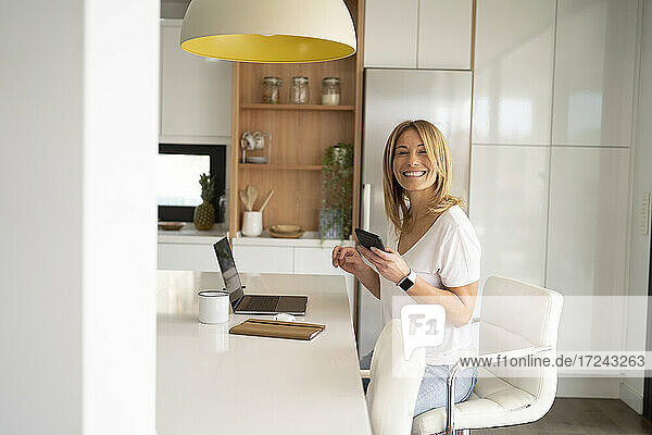 Female freelancer with smart phone in kitchen at home