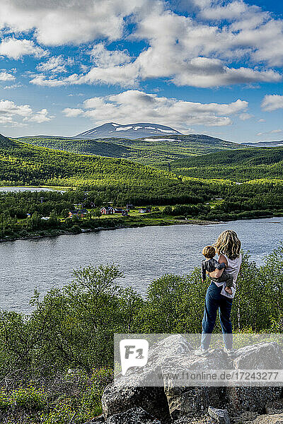 Mother admiring view of Karasjohka river with baby son in hands