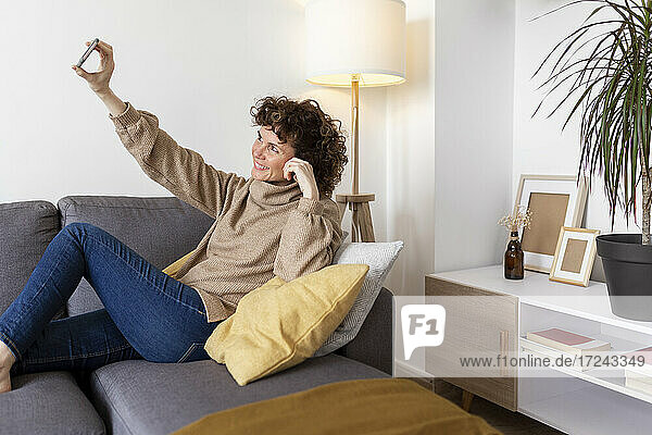 Fröhliche Frau  die ein Selfie mit ihrem Smartphone macht  während sie zu Hause auf dem Sofa sitzt