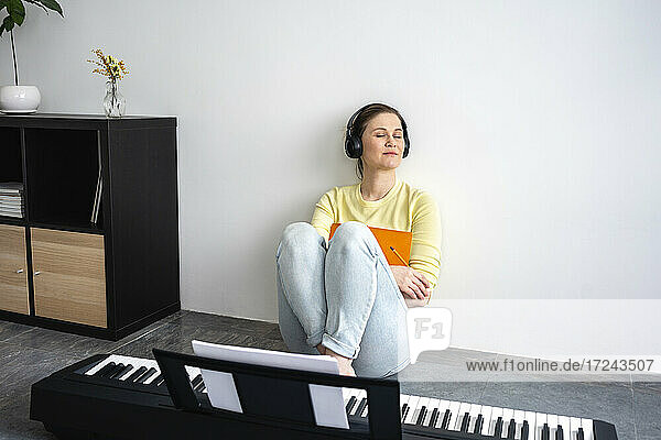Schöne Frau mit Kopfhörern hört Musik  während sie sich zu Hause an die Wand lehnt