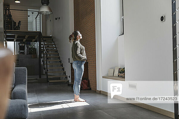Sunlight falling on woman standing in living room at home