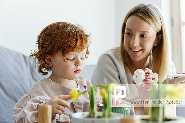 Lächelnde Mutter zeigt ihrer Tochter zu Hause ein Osterei