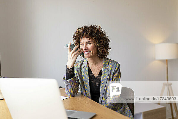 Lächelnde Freiberuflerin  die bei der Arbeit zu Hause eine Voicemail über ihr Smartphone verschickt