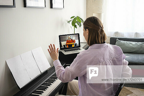 Mid adult woman learning piano with online tutorial on laptop at home
