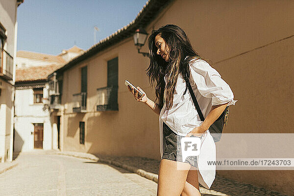 Young woman using mobile phone while standing with backpack on sunny day