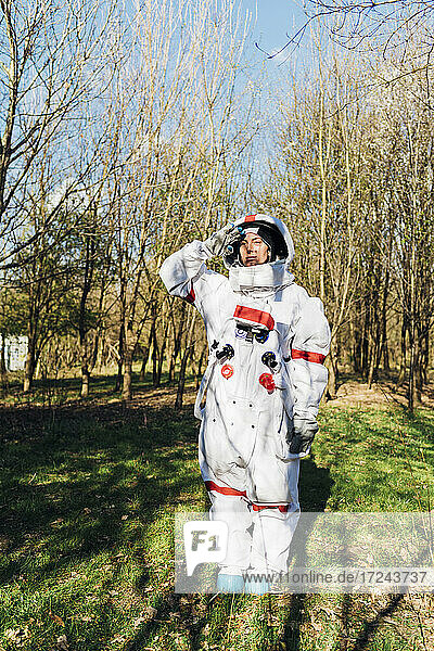 Junge Astronautin in Raumanzug und Helm grüßt im Wald stehend