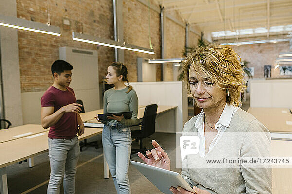 Unternehmerin  die ein digitales Tablet benutzt  während sich Fachleute im Büro unterhalten