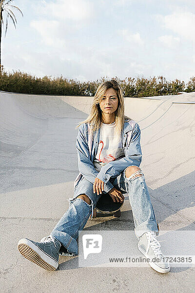 Woman wearing ripped jeans sitting in skateboard park