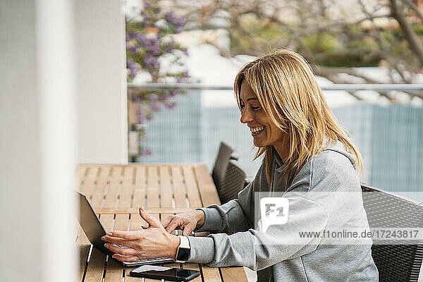 Lächelnde Berufstätige mit Laptop auf dem Balkon zu Hause