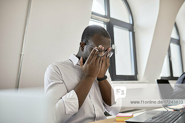 Müder männlicher Unternehmer  der sich die Augen reibt  während er im Büro sitzt