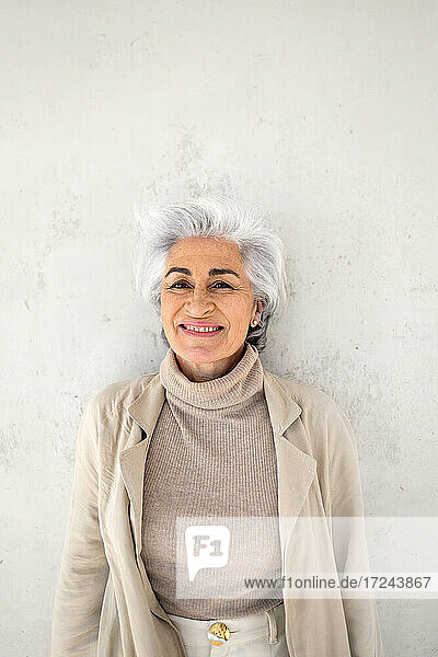 Mature woman smiling while standing in front of wall