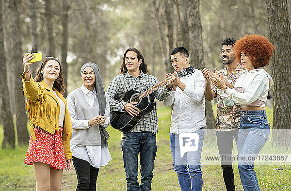 Woman taking selfie on smart phone with multi-ethnic friends in forest
