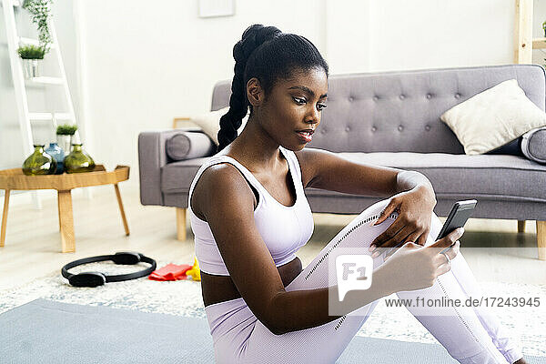 Young woman in sports clothing using smart phone while sitting at home