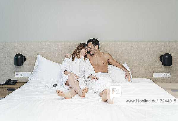 Man with arm around embracing woman sitting on bed in hotel room