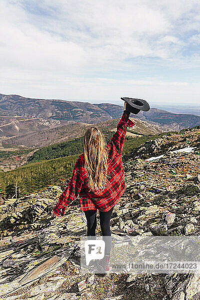 Frau mit erhobenem Arm und Hut auf einem Berg