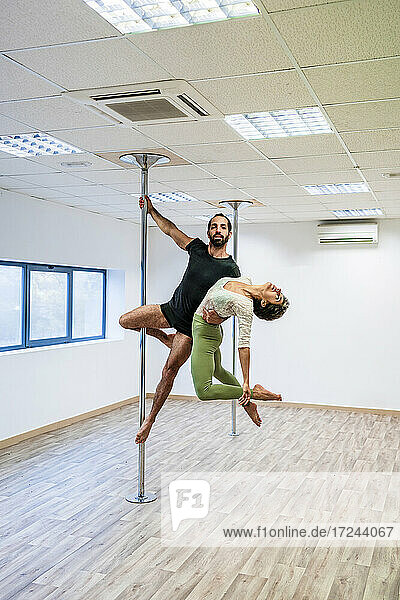 Männlicher Akrobat  der eine Tänzerin trägt  während er an einer Stange im Tanzstudio hängt