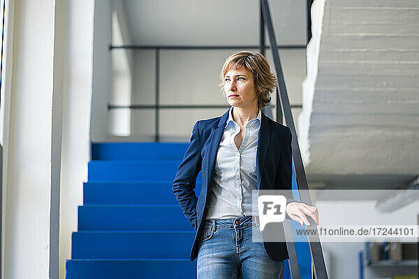Thoughtful female owner standing by steps railing in factory