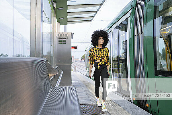 Junge Frau mit Laptop auf dem Bahnsteig eines Bahnhofs