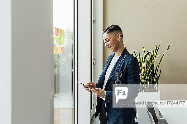 Smiling entrepreneur using digital tablet by window in office
