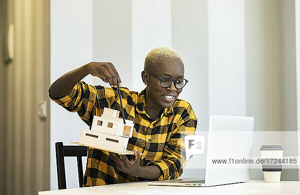Lächelnde Architektin  die ein Modell während einer Videokonferenz über einen Laptop zu Hause erklärt
