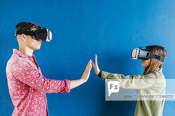 Freunde mit Virtual-Reality-Headset strecken einander die Hände an der blauen Wand entgegen