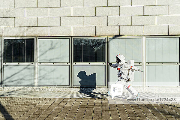 Weibliche Astronautin  die an einem sonnigen Tag vor einem Gebäude in der Stadt spazieren geht