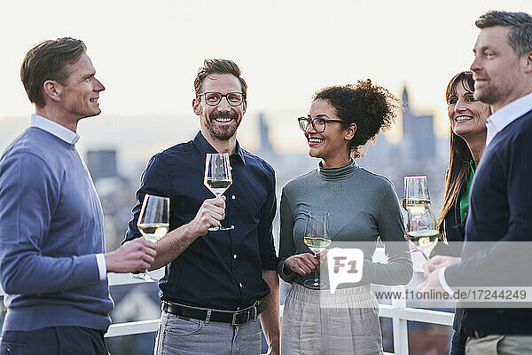 Lächelnde männliche und weibliche Unternehmer stehen mit Weingläsern auf der Terrasse eines Gebäudes