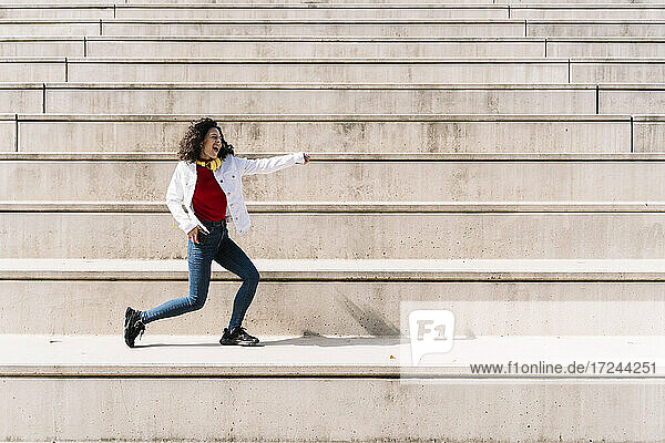 Carefree woman with headphones dancing on staircase during sunny day