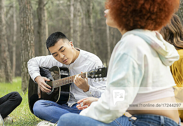 Mann spielt Gitarre  während er mit Freunden beim Picknick im Wald sitzt