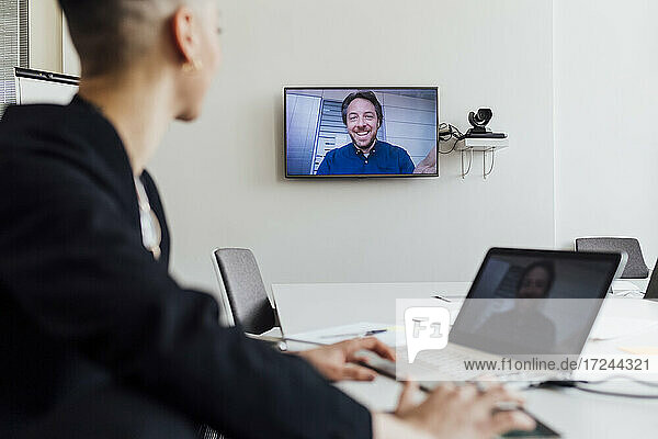 Geschäftsfrau  die an einer Besprechung mit einem Kollegen per Videoanruf über Laptop und Fernseher im Büro teilnimmt