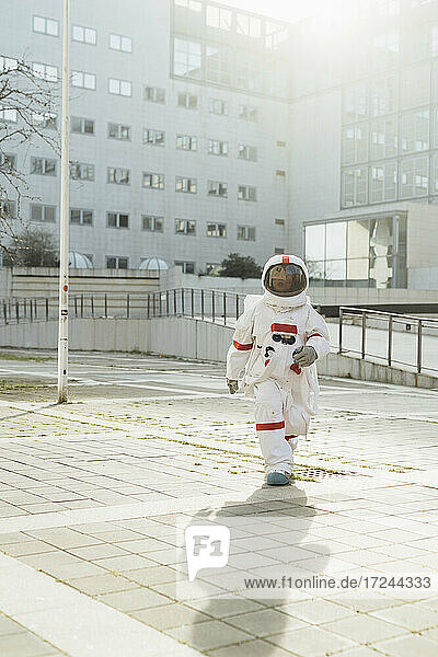 Junge Astronautin im Raumanzug  die an einem sonnigen Tag vor einem Gebäude spazieren geht