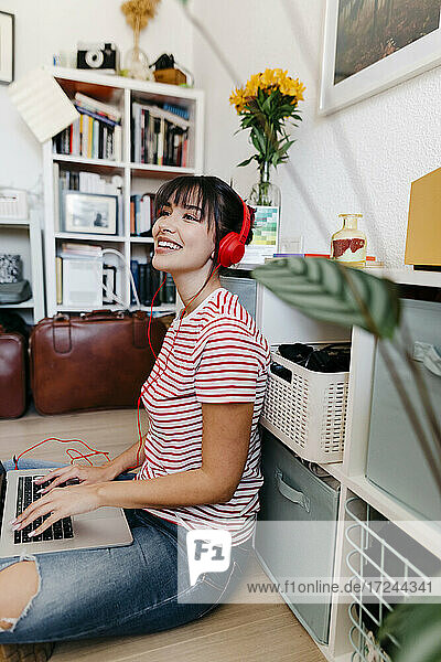 Schöne Frau mit Kopfhörern und Laptop sitzt im Wohnzimmer